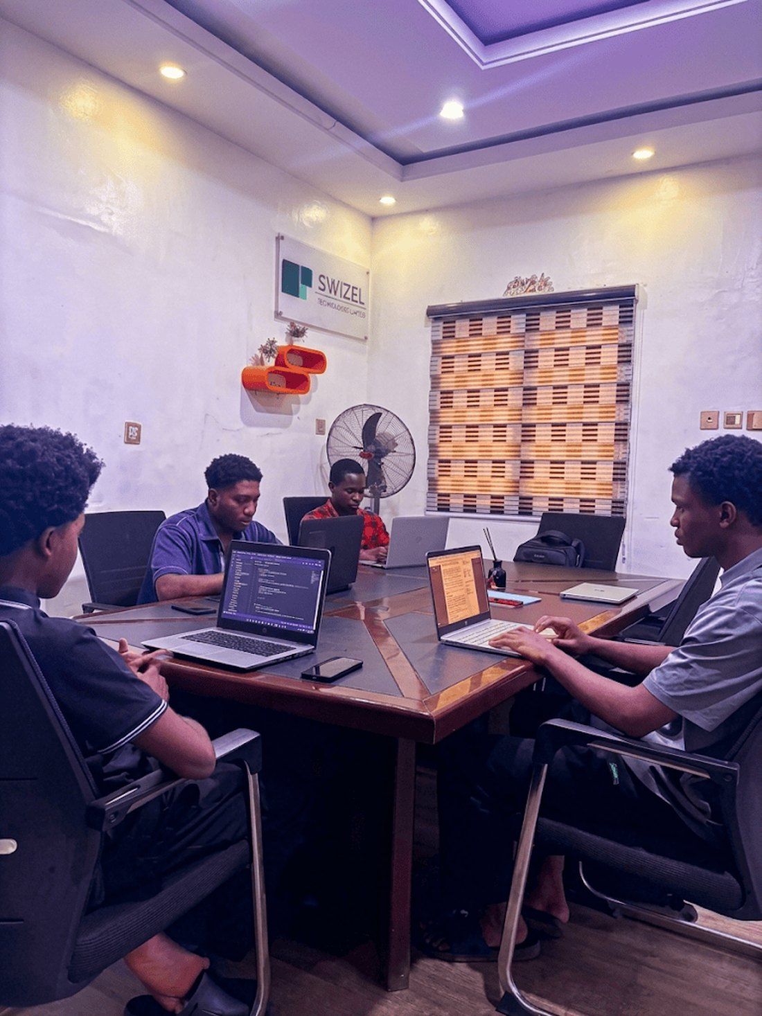 Trainees at the long table in the Swizel training room, working on real products